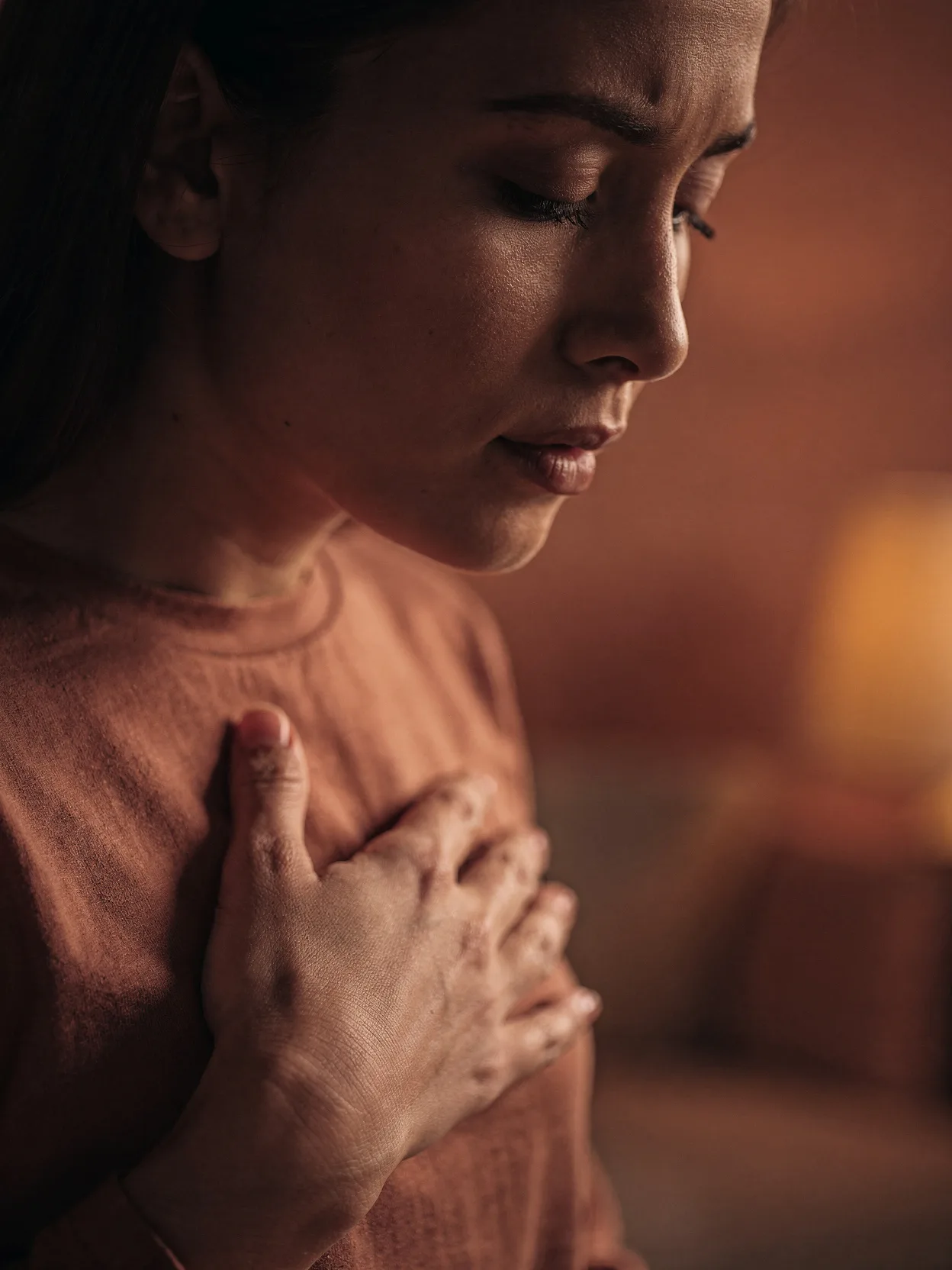 A woman in warm firelight, eyes closed, hand resting over her heart
