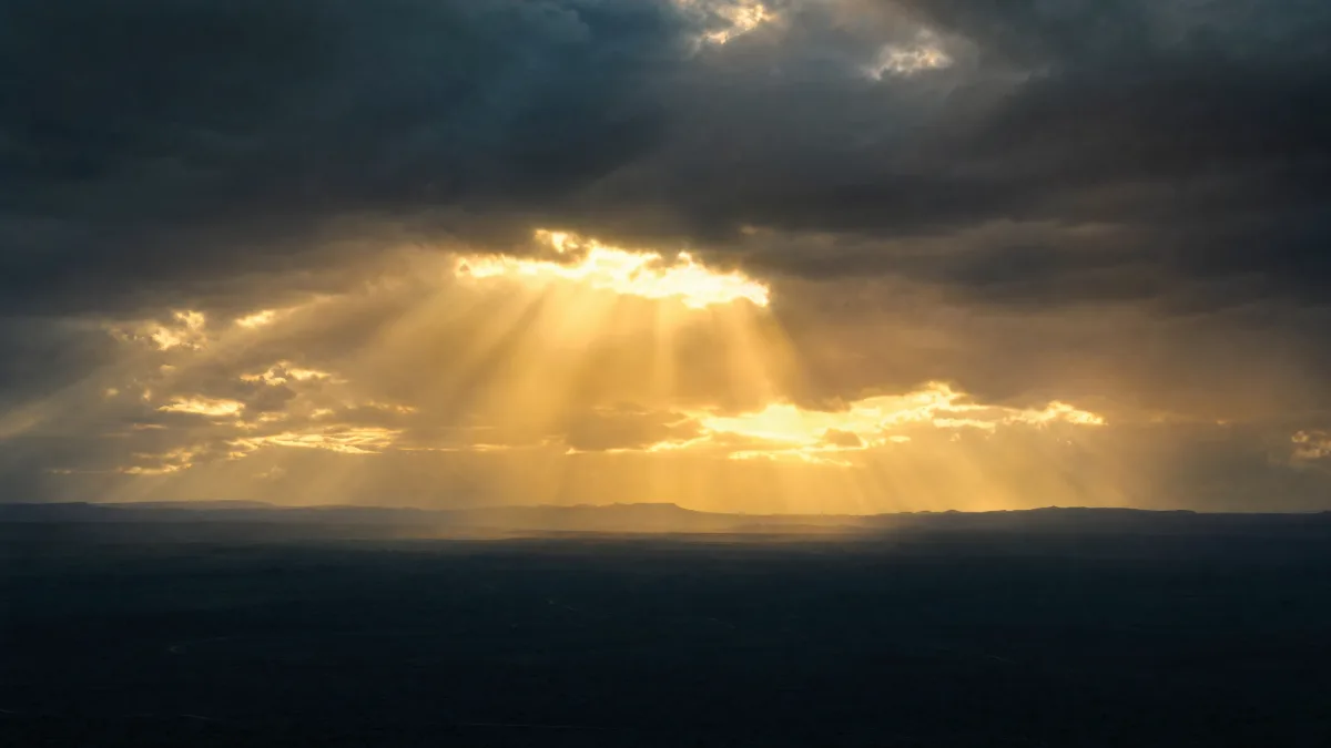 First sunlight breaking through heavy cloud cover over an open horizon